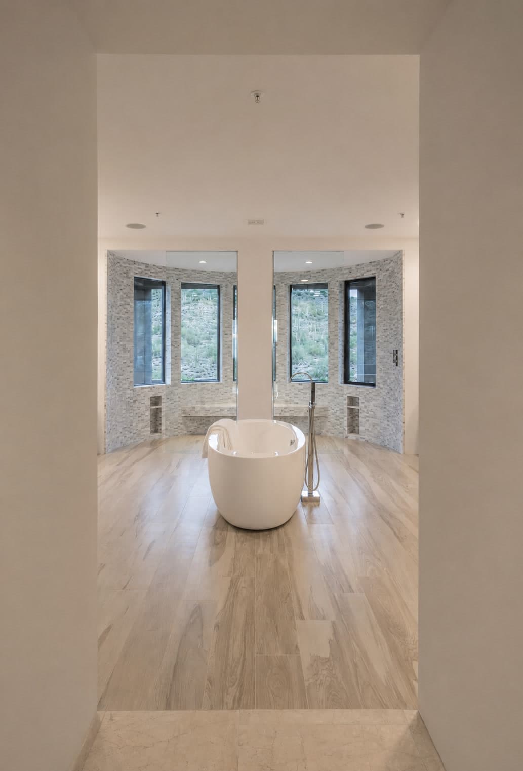 Luxury primary bathroom with a white freestanding soaking tub, mosaic walk-in showers, and desert views from an Apollo Builders remodel